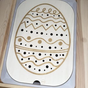 Könnte beinhalten: Ein weißes, eiförmiges Tablett aus Holz mit einem braunen und schwarzen geometrischen Muster. Das Tablett hat ein kleines Loch im Boden.
