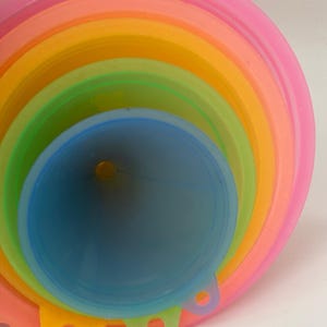 Könnte beinhalten: Ein Satz bunter Silikondeckel in Regenbogenfarben. Die Deckel sind ineinander verschachtelt und haben jeweils einen kleinen Griff.