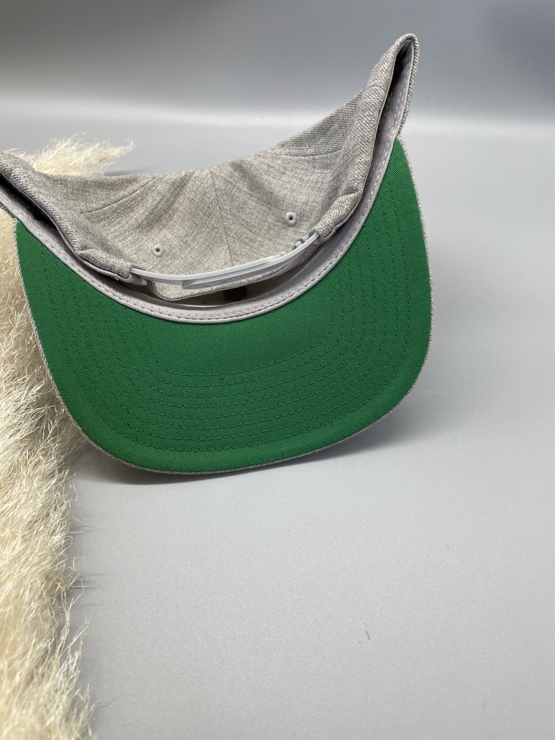 May include: A gray and green baseball cap with a green underside. The cap has a curved brim and a flat top.
