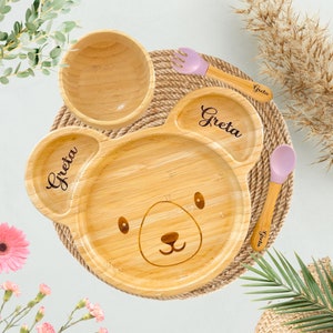 It is a personalised bamboo bear plate. The first name is engraved on its left ear, and the last name is engraved on its right ear with a customisable font style. Baby's first name is engraved on the handle of the bamboo spoon and fork.