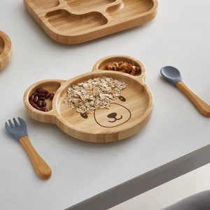 Bambo Plate Bear Shape is on the table with a spoon and fork made from bamboo and food-grade BPA Free silicone which included in the weaning set