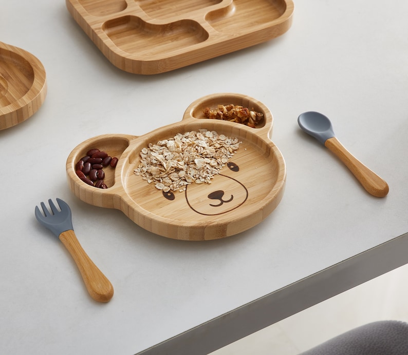 Bambo Plate Bear Shape is on the table with a spoon and fork made from bamboo and food-grade BPA Free silicone which included in the weaning set