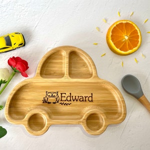 Puede incluir: Un plato dividido en forma de coche de madera con una cuchara de silicona gris. El plato está grabado con el nombre "Edward" y un pequeño diseño de búho.