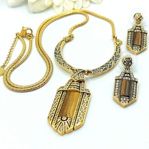 May include: A gold-toned jewelry set featuring a necklace, bracelet, and earrings. The necklace has a pendant with a rectangular tiger's eye stone, and the earrings match the pendant design. The set is embellished with clear crystals.