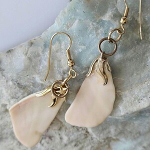 Peut inclure: Une paire de boucles d'oreilles en or avec un motif floral délicat et un pendentif en coquille blanche. Les boucles d'oreilles sont faites avec un crochet en or et un petit anneau en or.