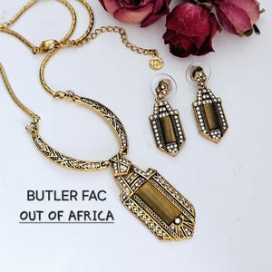 May include: A gold-toned necklace and matching earrings set with a geometric design. The necklace features a pendant with a rectangular center and is embellished with clear crystals. The earrings have a similar design. The text "BUTLER FAC OUT OF AFRICA" is visible.