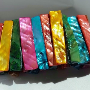 Peut inclure: Un bracelet coloré composé de pièces rectangulaires de coquille irisée. Le bracelet est composé de nuances de rouge, orange, jaune, vert, bleu et violet.
