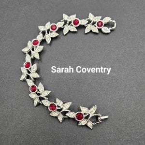 May include: A silver bracelet with a floral design featuring red and clear rhinestones. The bracelet has a clasp closure.