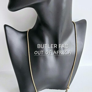 May include: Gold-toned necklace and matching earrings set displayed on a black mannequin. The jewelry features rectangular pendants with a brown center stone and ornate detailing. The text "BUTLER FAC OUT OF AFRICA" is visible.