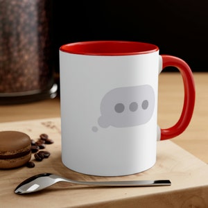 May include: White ceramic mug with a red rim and handle. The mug features a gray thought bubble with three gray dots inside.