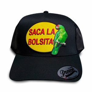 May include: Black trucker hat with a yellow circle patch that says "SACA LA BOLSITA" in red and black lettering. A green parrot is perched on a branch on the patch. The hat has a black mesh back and a black Provok label on the back.