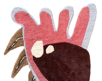 May include: A pink and brown abstract rug with a unique, organic shape. The rug has a fluffy texture and features a large brown shape in the center.