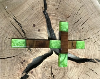 May include: A wooden cross with green resin inlay. The cross is made of dark wood and has a light green resin inlay. The cross is sitting on a wooden surface.