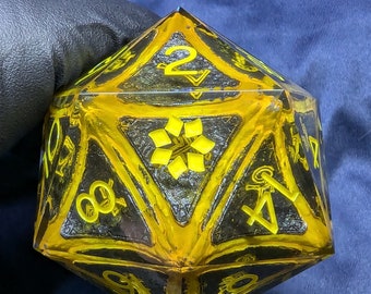 Può includere: Un dado da 20 facce nero e giallo con un design a stella su un lato. Il dado è fatto di resina trasparente con un motivo a spirale nero e giallo.