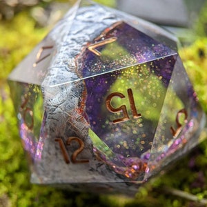 May include: A clear, iridescent, purple and white resin d20 dice with copper numbers. The dice has a glittery, sparkly finish.