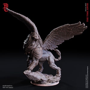 May include: A detailed, grey, sculpted figurine of an Androsphinx, a winged lion with a human head, standing on a rocky base. The figurine is posed with its wings spread and its head turned to the side, as if roaring. The figurine is 50 mm in size.