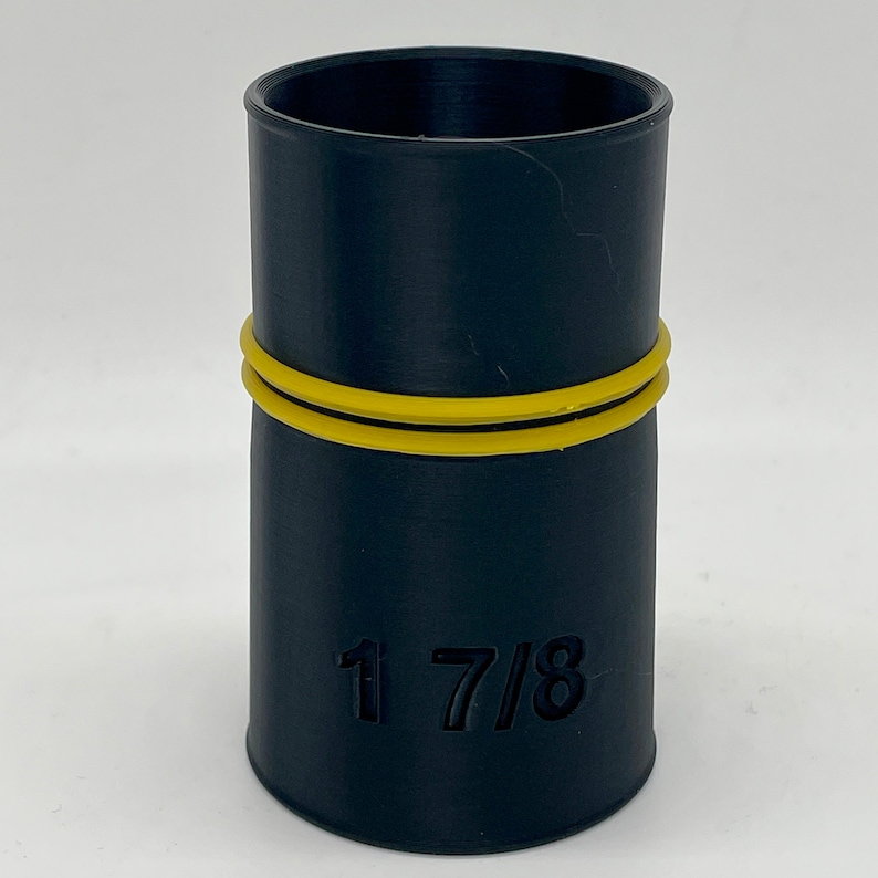 Puede incluir: Un accesorio cil&iacute;ndrico negro con una banda amarilla. El n&uacute;mero "1 7/8" est&aacute; grabado en el lateral. Este componente de fontaner&iacute;a se utiliza probablemente para conectar tuber&iacute;as u otros accesorios.