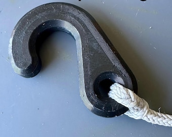 May include: A black, J-shaped hook with a textured, layered surface finish. The hook features a circular opening at the base through which a thick, light gray braided rope is threaded. The design is simple, functional, and industrial in appearance.