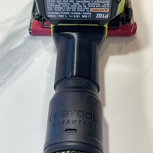以下が含まれることがあります： 側面にある「FESTOOL CLEANTEC」の文字が入った、黒と緑の電動工具アタッチメント。アタッチメントは、「P102 LI-ION 18 V」と「1.3Ah/24Wh」の文字が入った黒と黄色の電動工具に接続されています。