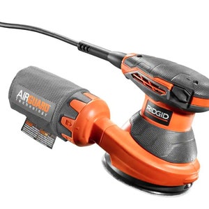 May include: An orange and black Ridgid random orbit sander with a black power cord. The sander has a round base and a dust collection bag with "AIR GUARD TECHNOLOGY" printed on it. The Ridgid logo is visible on the top of the sander.