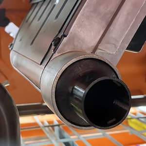 May include: Close-up of a metallic, industrial-style object with a cylindrical, black nozzle. The object has a rectangular body with a slightly weathered appearance. The nozzle is surrounded by a dark, circular band.