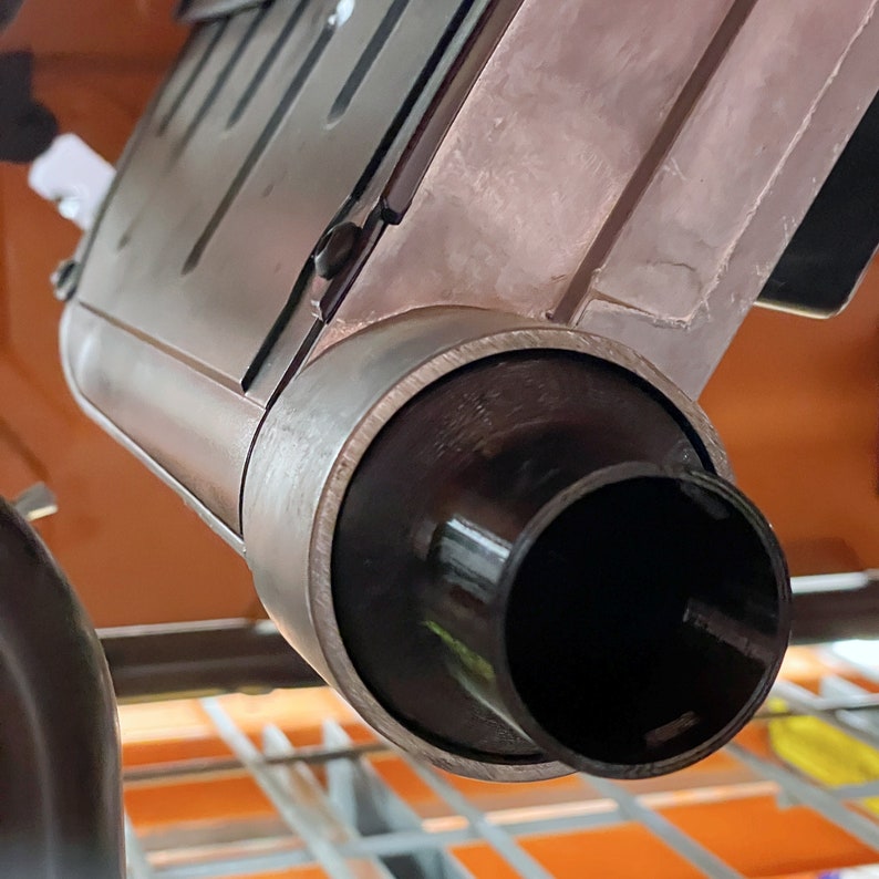 May include: Close-up of a metallic, industrial-style object with a cylindrical, black nozzle. The object has a rectangular body with a slightly weathered appearance. The nozzle is surrounded by a dark, circular band.