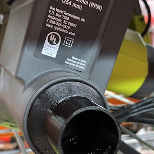 Puede incluir: Primer plano de un puerto de recogida de polvo de sierra de mesa negro. La etiqueta de la sierra indica que es un modelo RTS12, hoja de 254 mm, 120V y 15A. La etiqueta tambi&eacute;n incluye la informaci&oacute;n de contacto del fabricante y la certificaci&oacute;n UL.