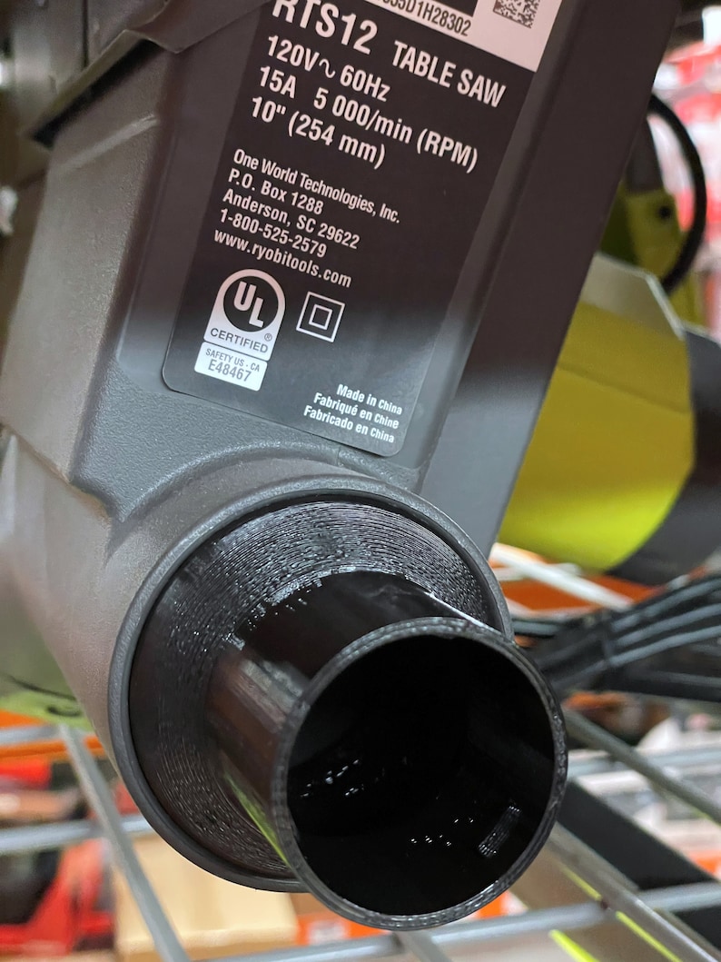 Puede incluir: Primer plano de un puerto de recogida de polvo de sierra de mesa negro. La etiqueta de la sierra indica que es un modelo RTS12, hoja de 254 mm, 120V y 15A. La etiqueta tambi&eacute;n incluye la informaci&oacute;n de contacto del fabricante y la certificaci&oacute;n UL.