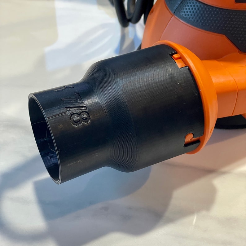 May include: A black 3D-printed attachment for a power tool, featuring the number "18" on the side. The attachment is connected to an orange and black power tool.