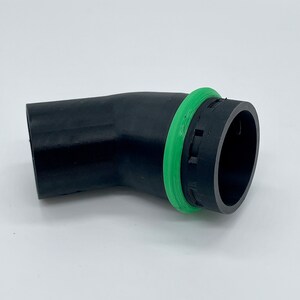 May include: A black, curved automotive part with a green circular seal. The part has a textured surface and a cylindrical opening on one end. The green seal is a bright, contrasting color against the black.