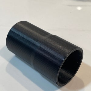 K&ouml;nnte beinhalten: Ein schwarzer zylindrischer Adapter mit strukturierter Oberfl&auml;che. Der Adapter hat an einem Ende eine breitere und am anderen Ende eine schmalere &Ouml;ffnung. Das Objekt besteht aus einem festen, dunklen Material.