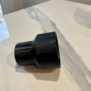K&ouml;nnte beinhalten: Ein schwarzer Kunststoffadapter mit einem ausgestellten, zylindrischen Design. Der Adapter hat an einem Ende eine breitere &Ouml;ffnung und am anderen Ende eine schmalere &Ouml;ffnung, die durch einen konischen Abschnitt verbunden sind. Das Objekt wird wahrscheinlich zum Verbinden von Rohren oder Schl&auml;uchen unterschiedlicher Gr&ouml;&szlig;e verwendet.