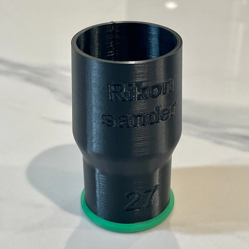 Puede incluir: Objeto cil&iacute;ndrico negro con el texto "Rikon Sander" y el n&uacute;mero "27" impresos. La base tiene un anillo verde. El objeto parece estar impreso en 3D.