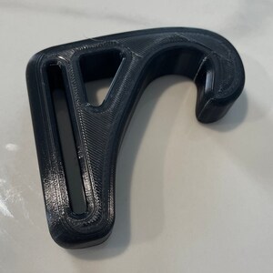 May include: Black 3D-printed hook with a curved design and a rectangular opening. The hook has a textured surface and is likely used for hanging items. The overall shape is reminiscent of a question mark.