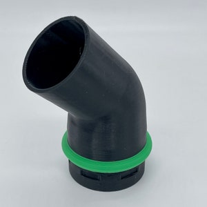 May include: A black, angled pipe fitting with a green O-ring seal. The fitting has a curved design and a cylindrical opening. The object is made of a matte black material and is likely a component for plumbing or machinery.