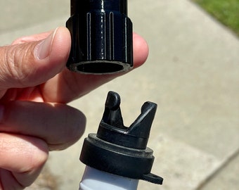 May include: A black plastic cylindrical connector cap with vertical ridges and a notched top, positioned above a matching black plastic locking mechanism attached to a white ribbed hose, designed for secure attachment and alignment.