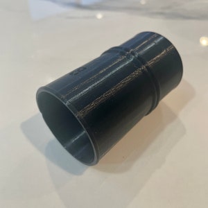 Puede incluir: Adaptador de pl&aacute;stico cil&iacute;ndrico negro con un dise&ntilde;o acanalado. El adaptador tiene una abertura ligeramente ensanchada en un extremo y una abertura m&aacute;s peque&ntilde;a en el otro. La superficie tiene un aspecto texturizado.