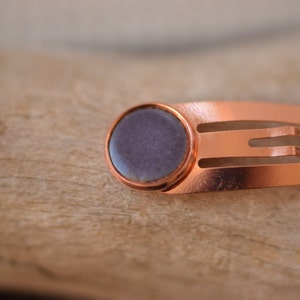 May include: A copper hair clip with a round, purple, resin cabochon.