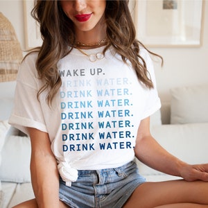 May include: White t-shirt with the text "WAKE UP. DRINK WATER." repeated in a gradient of blue.