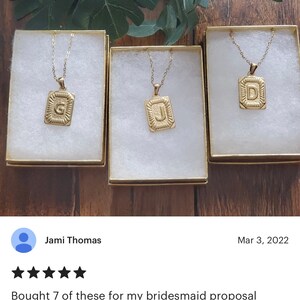 Op de afbeelding: Drie goudkleurige kettingen met initialen hangers in een vierkante vorm. De initialen zijn G, J en D. De kettingen worden gepresenteerd in witte doosjes met gouden randen.