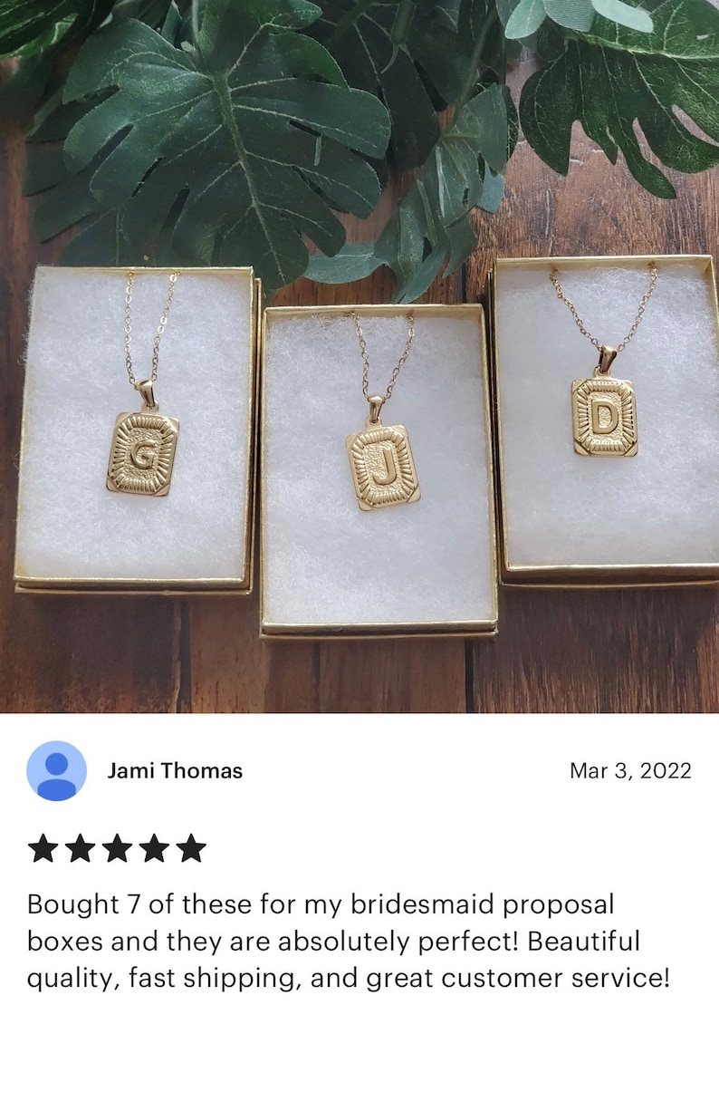 Op de afbeelding: Drie goudkleurige kettingen met initialen hangers in een vierkante vorm. De initialen zijn G, J en D. De kettingen worden gepresenteerd in witte doosjes met gouden randen.