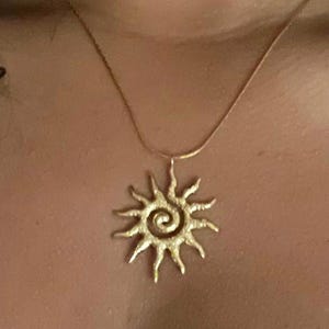 May include: A gold necklace with a sun pendant. The sun has a spiral design in the center.