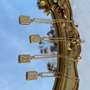 May include: Four gold necklaces with square pendants featuring the letters P, U, D, and O. The necklaces are hanging from a gold-framed mirror.