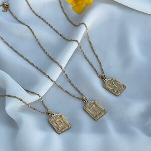 May include: Three gold necklaces with initial pendants. The pendants are rectangular and have a raised, textured letter. The letters are D, T, and Y.