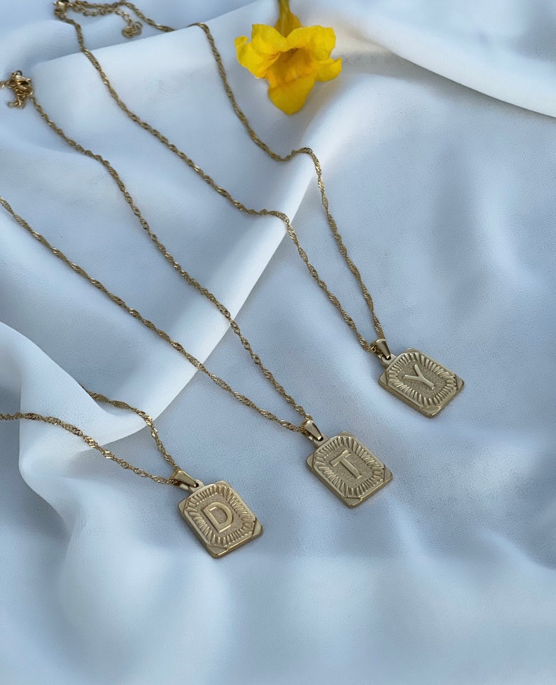 May include: Three gold necklaces with initial pendants. The pendants are rectangular and have a raised, textured letter. The letters are D, T, and Y.