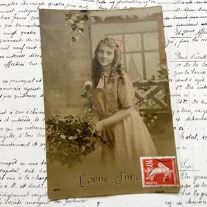 Década de 1910 - Postal con una joven, flores y la palabra "Bonne année" / "Feliz Año Nuevo".