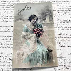 Década de 1910 - Postal con una joven, flores y la palabra "Heureuse fête"