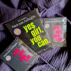 Könnte beinhalten: Drei Aufbügler in Klarsichtverpackung, jeweils mit dem Satz "Yes Girl, You Can." Der Text ist in leuchtendem Neongrün und Pink gehalten, mit den Worten auf schwarzem Hintergrund. Die Aufbügler sind DIY.
