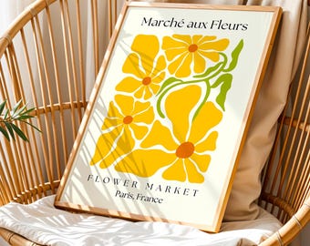 May include: A framed art print featuring a floral design with yellow flowers and green stems. The text "Marché aux Fleurs" and "Flower Market Paris, France" are printed on the off-white background. The artwork is displayed on a wicker chair.
