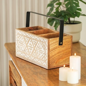 May include: A wooden organiser with three compartments and a black metal handle. The organiser has a white carved design and is sitting on a wooden surface with three white candles.
